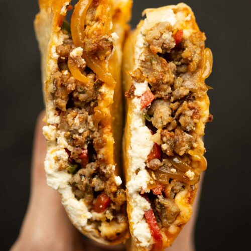 close up overhead shot of hand holding sausage peppers tortilla calzone sliced open