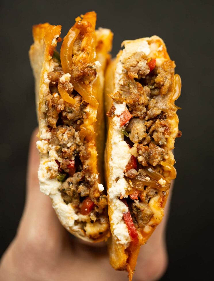 close up overhead shot of hand holding sausage peppers tortilla calzone sliced open