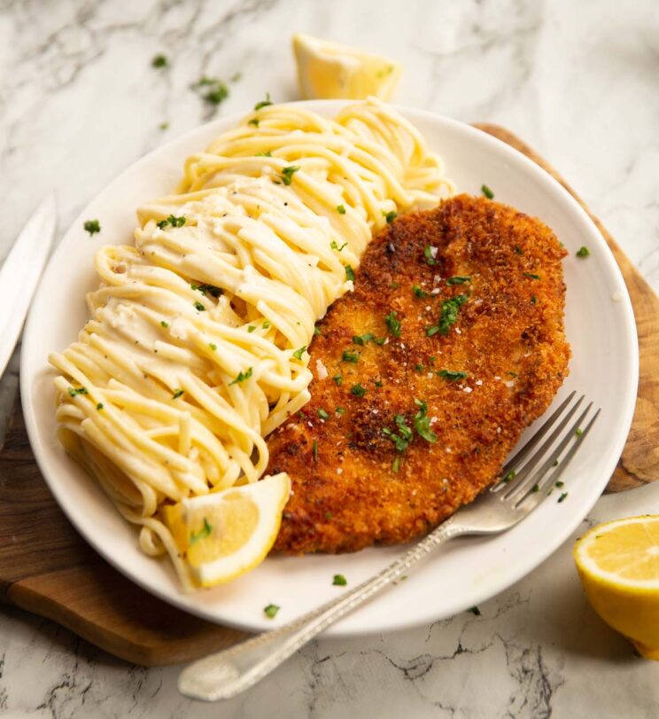 creamy lemon chicken pasta served on small white plate on wooden chopping board