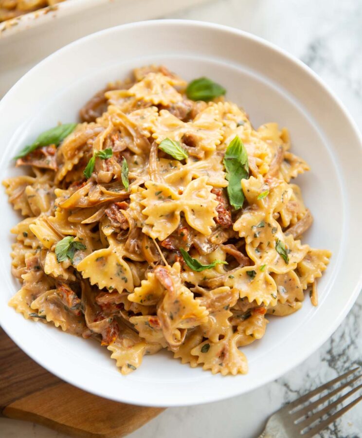 caramelised onion pasta in large white bowl on brown chopping board