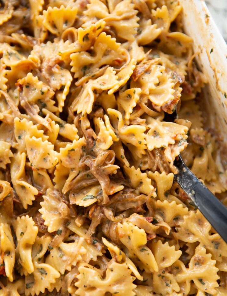 close up shot of caramelised onion pasta in large white baking dish with black serving spoon