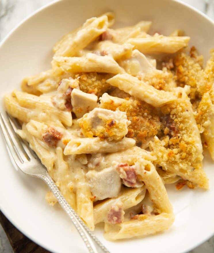 close up shot of chicken and bacon pasta bake served in large white dish