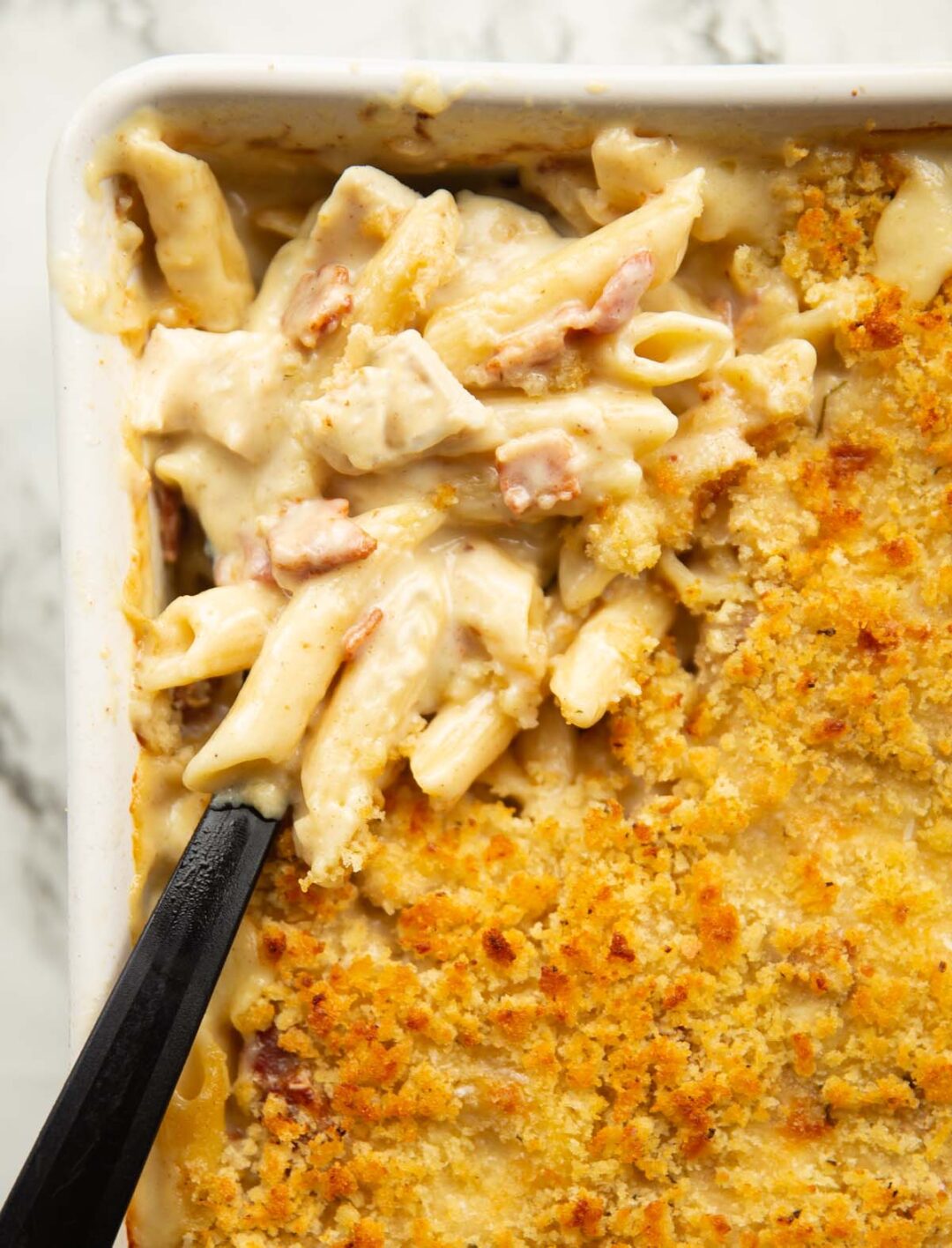 overhead close up shot of chicken bacon pasta bake with black serving spoon digging in