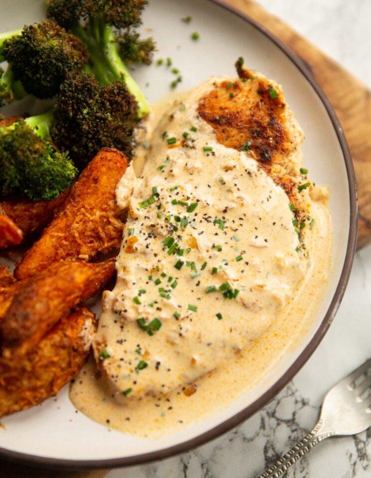 close up shot of cream cheese chicken on small white plate with broccoli and wedges