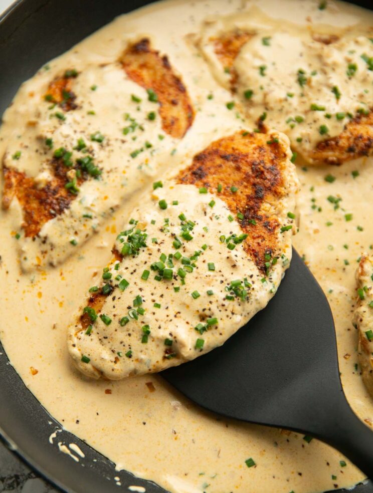 close up shot of spatula lifting chicken breast out of pan covered in cream cheese sauce