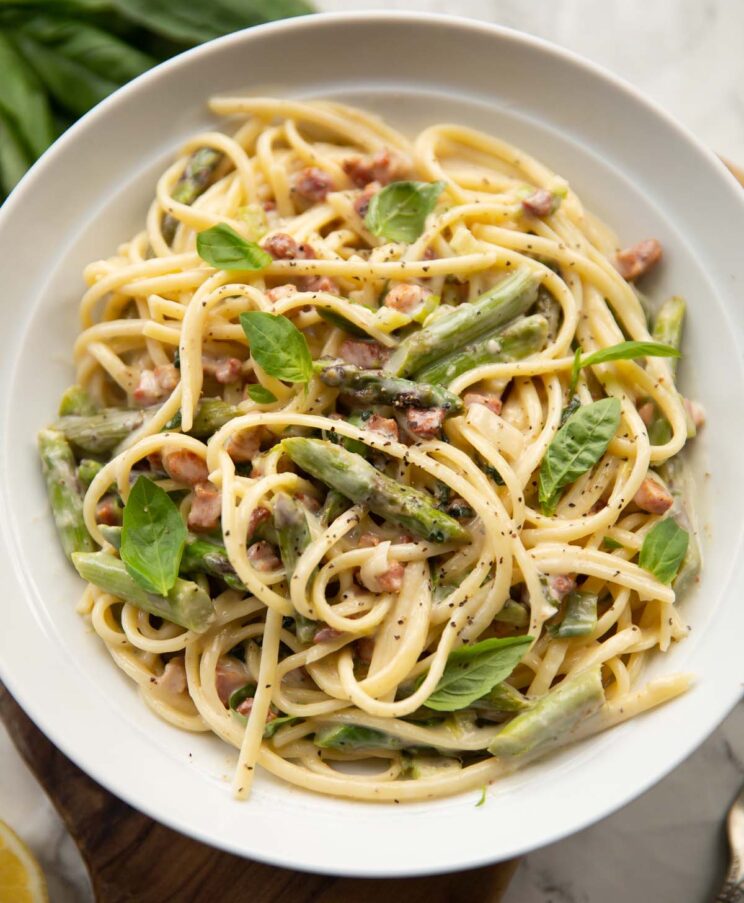 overhead shot of asparagus pancetta pasta in large white bowl garnished with fresh basil leaves