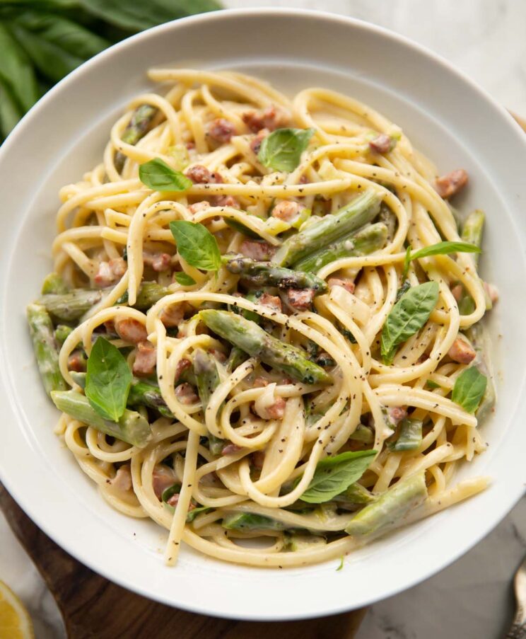 overhead shot of asparagus pancetta pasta in large white bowl garnished with fresh basil leaves