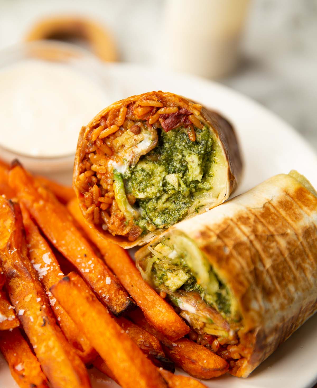 halved chicken pesto wrap on white plate with sweet potato fries