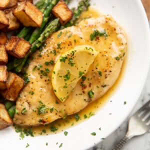 honey lemon chicken breast on small white plate with asparagus and roast potatoes