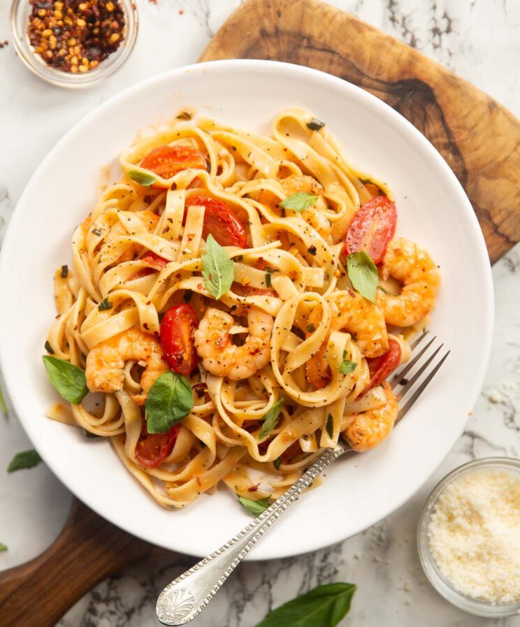 overhead shot of prawn tomato pasta on small white plate on wooden chopping board with silver fork