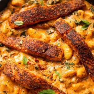 4 salmon fillets and gnocchi in large pan garnished with fresh basil