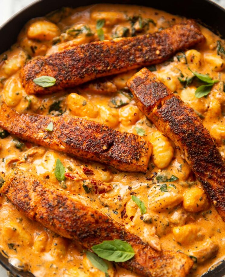 4 salmon fillets and gnocchi in large pan garnished with fresh basil