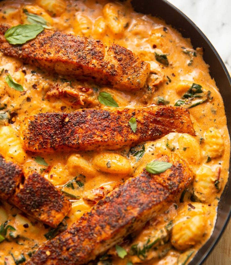close up shot of salmon gnocchi in large pan garnished with fresh basil