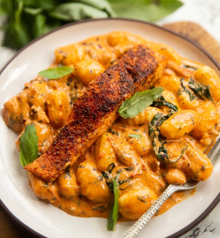 salmon and gnocchi served on small white plate with silver fork and fresh basil blurred in background