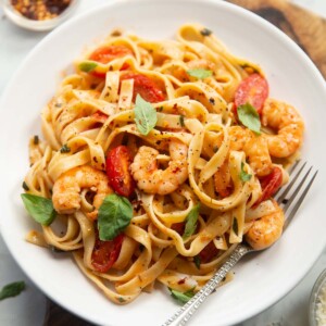 tomato and prawn pasta served on small white plate with silver fork
