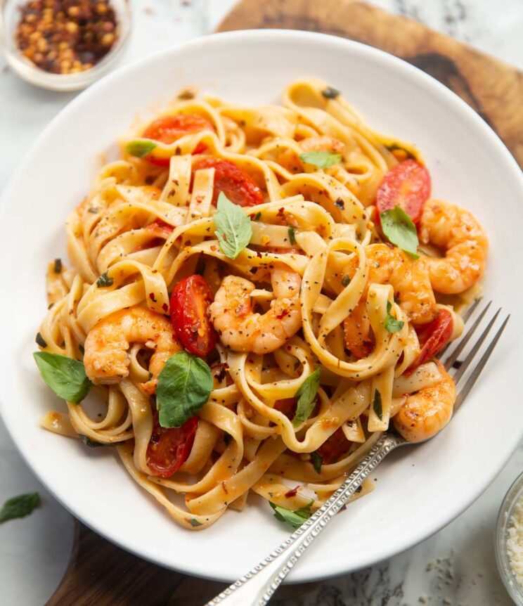 tomato and prawn pasta served on small white plate with silver fork