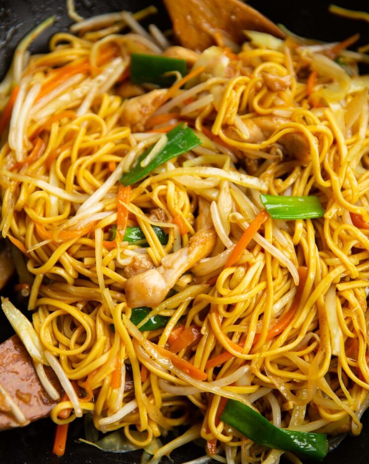 chicken chow mein in large wok with wooden spoons at the side