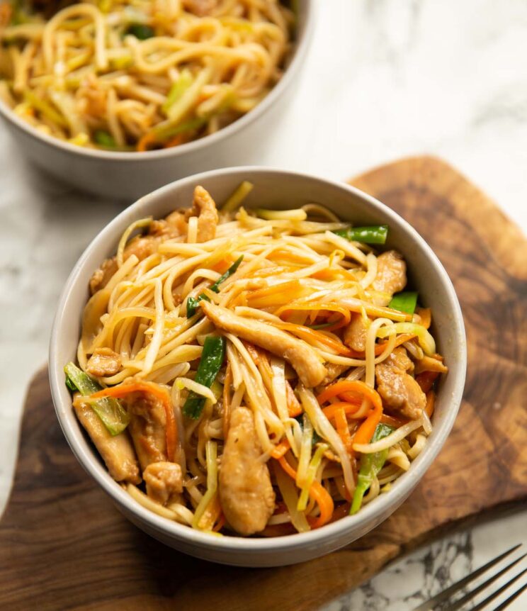 chicken chow mein in large grey bowl on chopping board with one more in the background