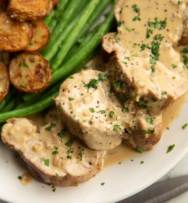 close up shot of pork tenderloin with boursin sauce garnished with parsley on small white plate