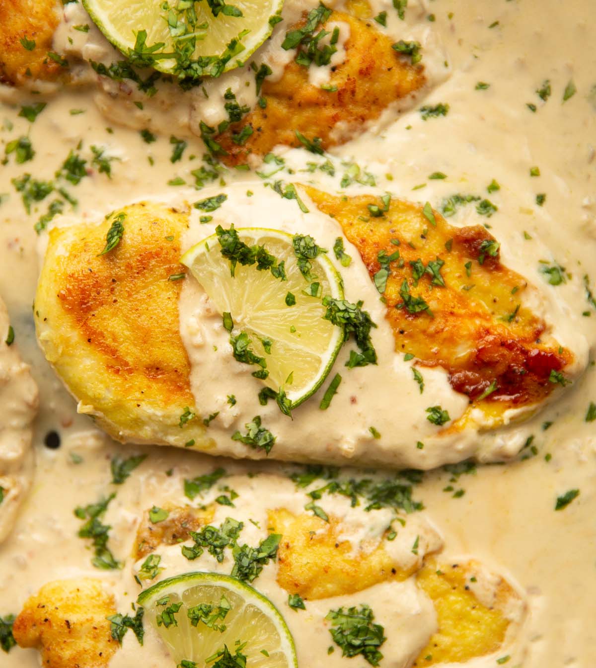 overhead close up shot of 3 creamy coconut lime chicken breasts in pan garnished with lime and coriander