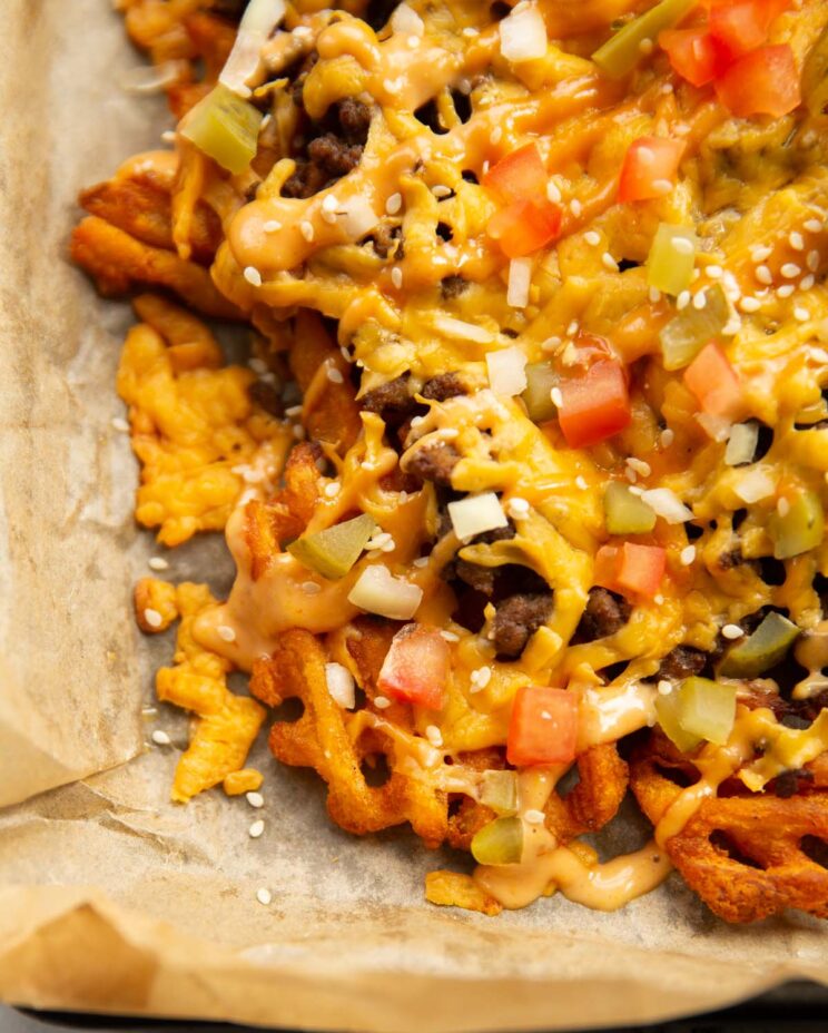 close up shot of loaded cheeseburger waffle fries on baking paper