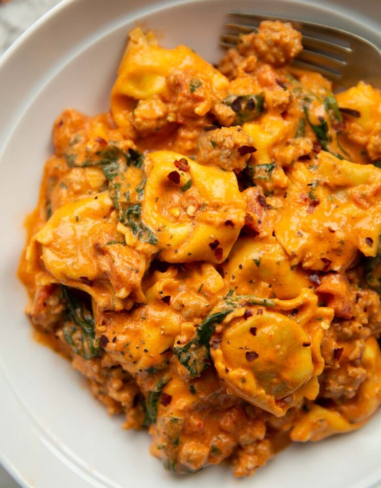 close up shot of sausage tortellini in large white bowl with silver fork