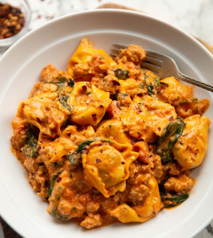 spicy sausage tortellini served in large white bowl with silver fork