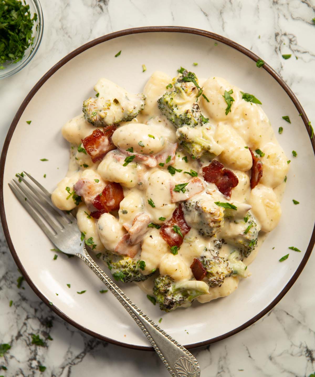 overhead shot of broccoli bacon boursin gnocchi on small white plate with silver fork