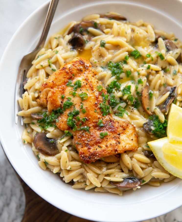 garlic butter chicken orzo served in large white bowl with fork and lemon wedges