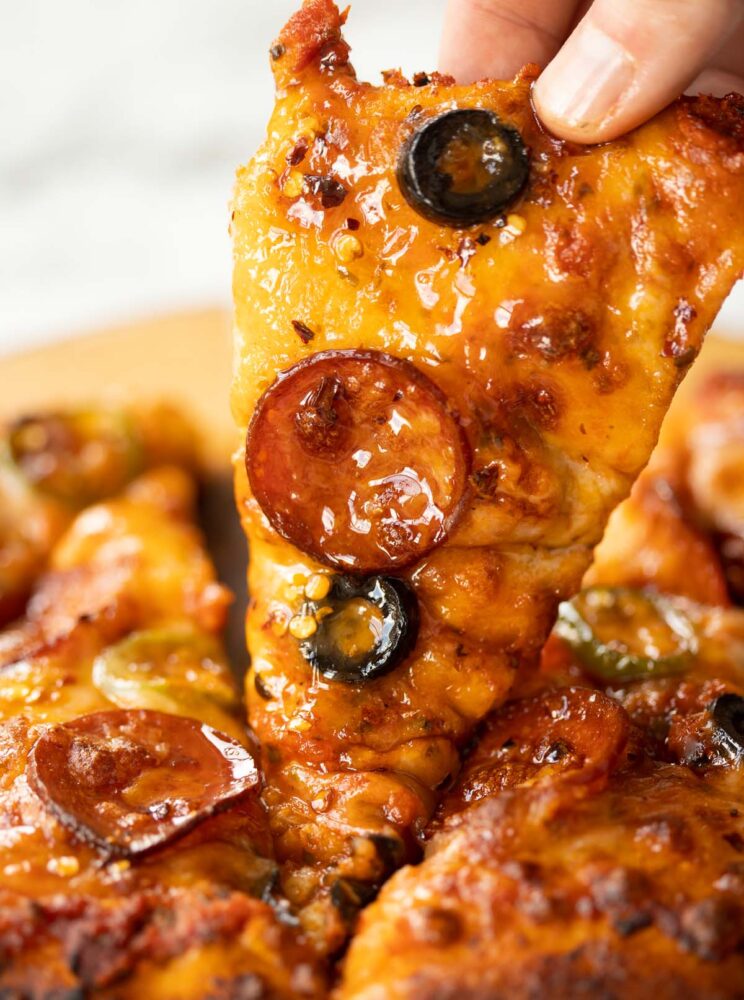 close up shot of fingers lifting slice of hot honey garlic flatbread pizza