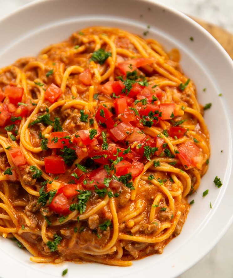 close up shot of taco spaghetti in large white dish with tomatoes and coriander