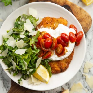 overhead shot of chicken milanese burrata on small white plate on wooden chopping board