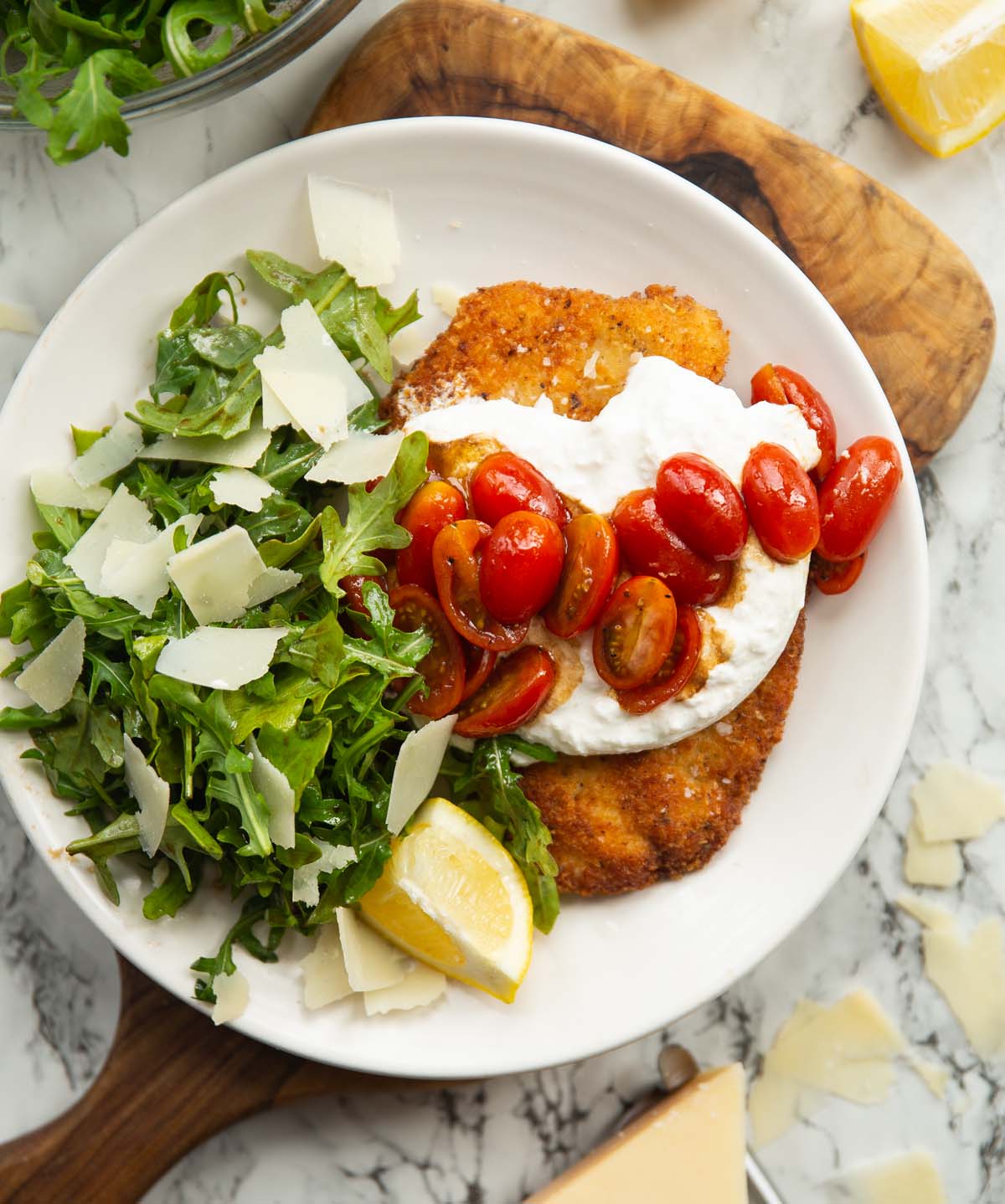 overhead shot of chicken milanese burrata on small white plate on wooden chopping board