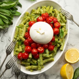 overhead shot of pistachio pesto pasta in large dish with tomatoes and burrata