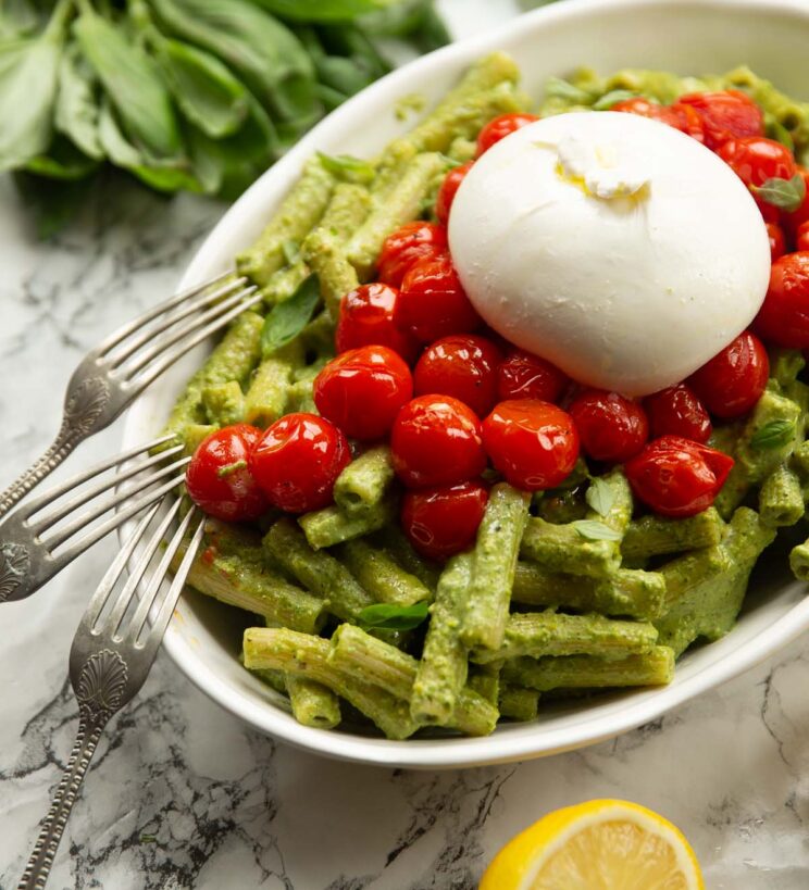 pistachio pesto pasta with tomatoes in large white dish with burrata