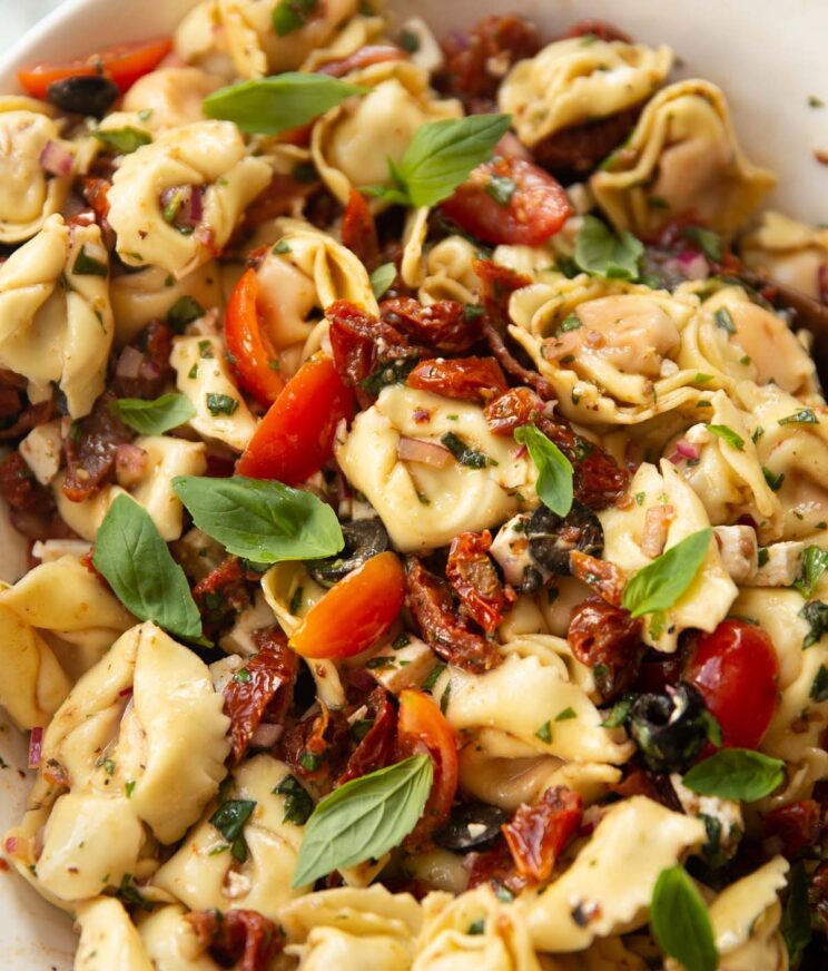 Sun dried tomato tortellini pasta salad in a large white bowl garnished with basil