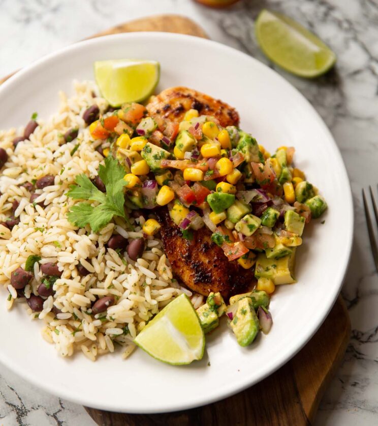 cajun chicken avocado salsa on small white plate with rice and lime wedges