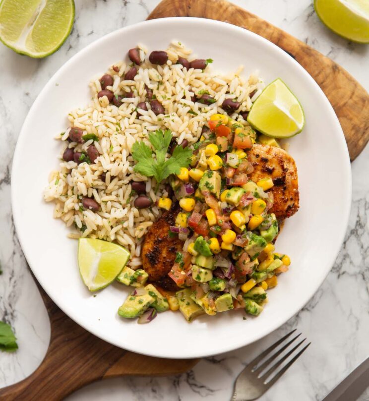 overhead shot of cajun chicken breast avocado salsa rice and black beans on small white plate