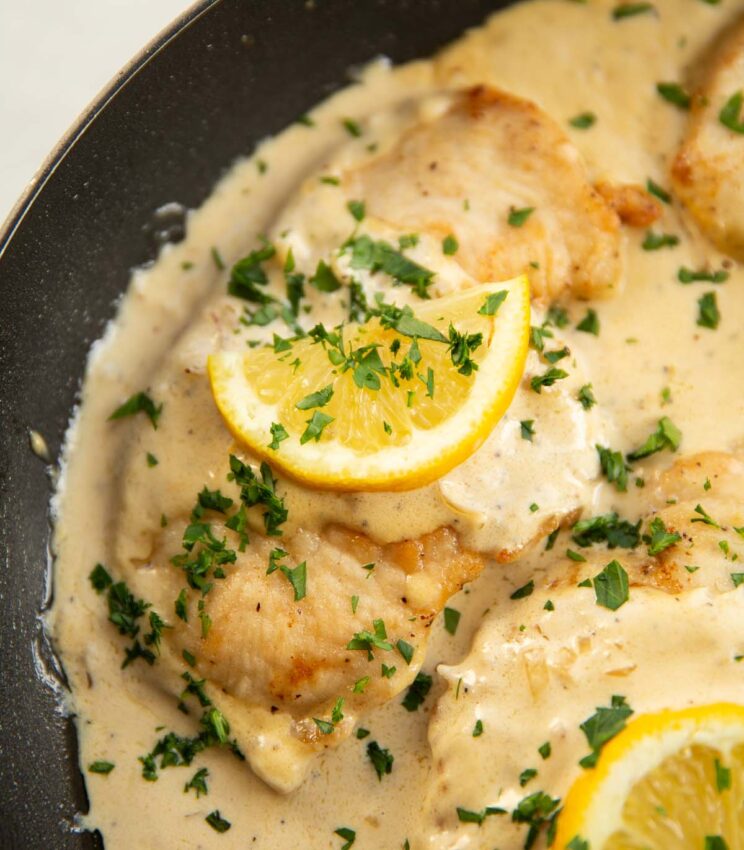 close up shot of creamy lemon chicken breast in pan garnished with fresh parsley