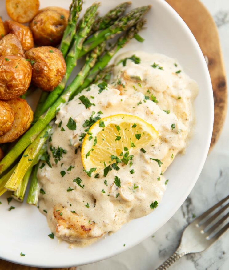 creamy lemon chicken served on small white plate with asparagus and baby potatoes