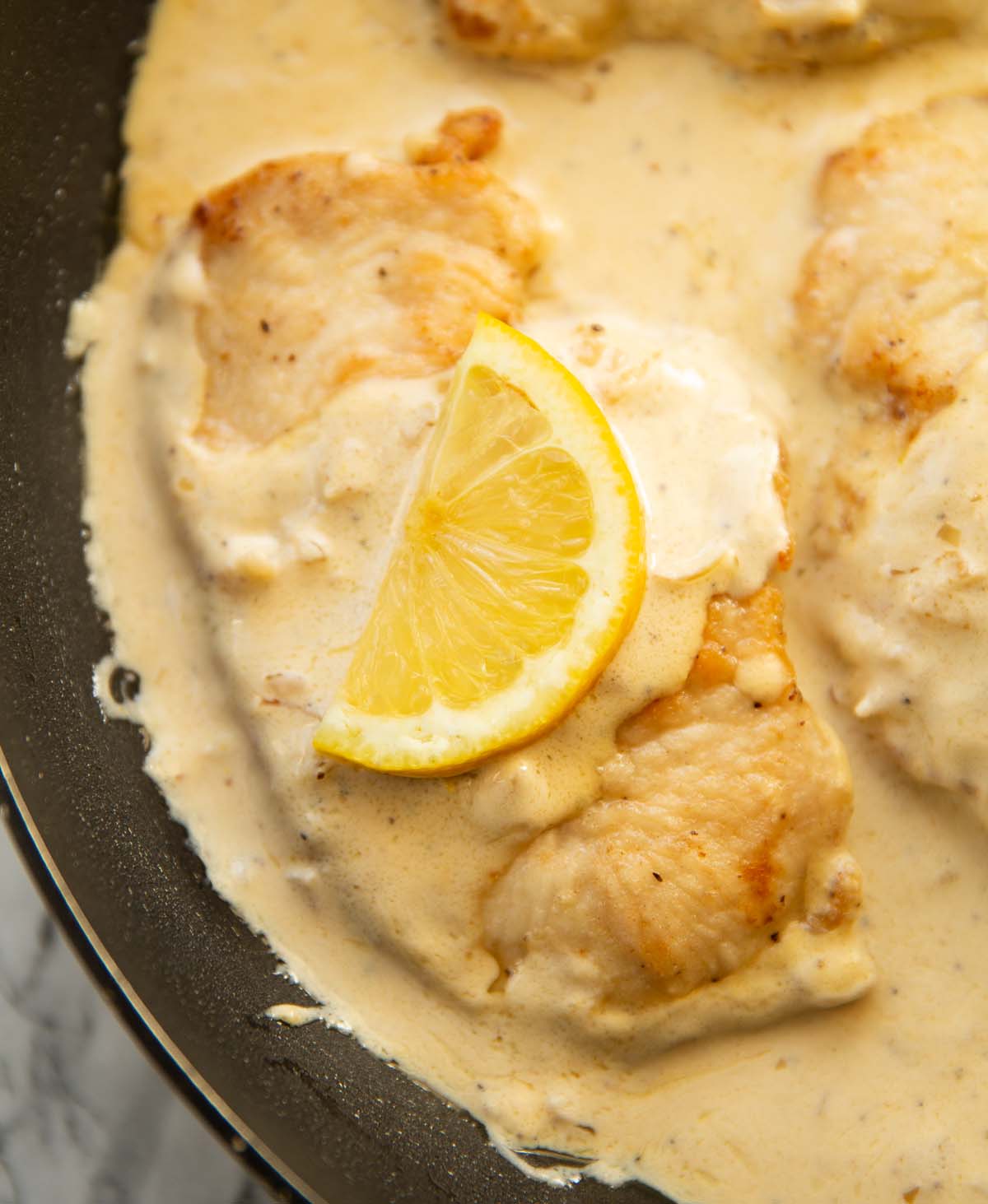 close up shot of creamy lemon chicken in pan with lemon wedge on top