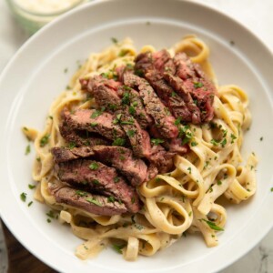 boursin steak pasta served in white bowl with pot of parsley and parmesan in background