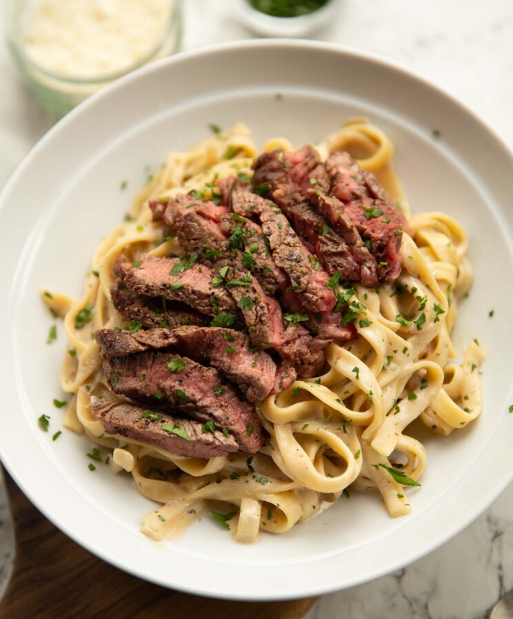 boursin steak pasta served in white bowl with pot of parsley and parmesan in background