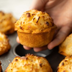 close up shot of hand holding mini cottage pie above muffin tin