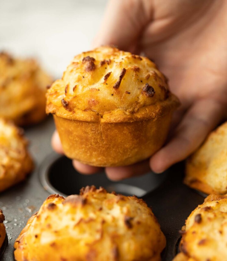 close up shot of hand holding mini cottage pie above muffin tin
