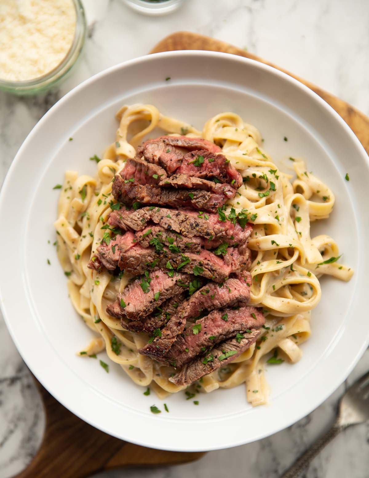 overhead shot of steak pasta in large white dish on wooden chopping board