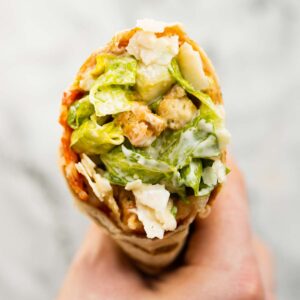 close up overhead shot of hand holding caesar salad pepperoni wrap