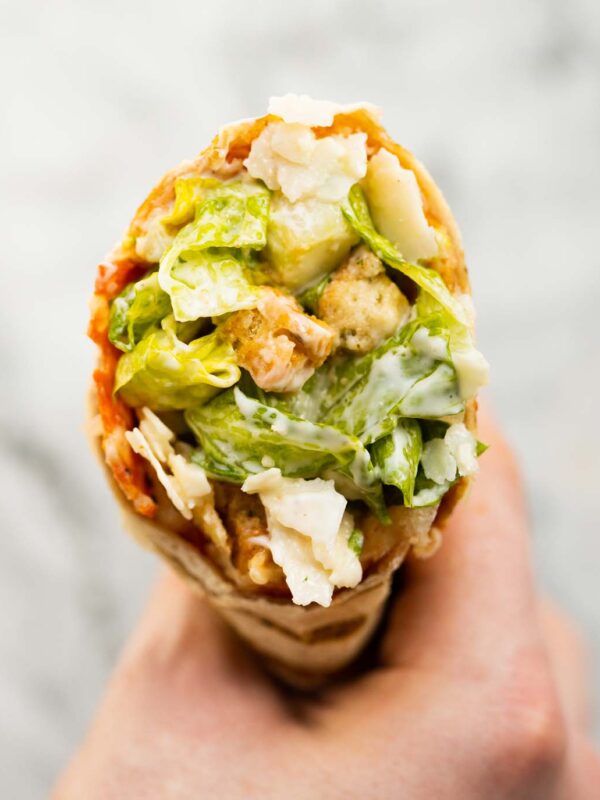 close up overhead shot of hand holding caesar salad pepperoni wrap