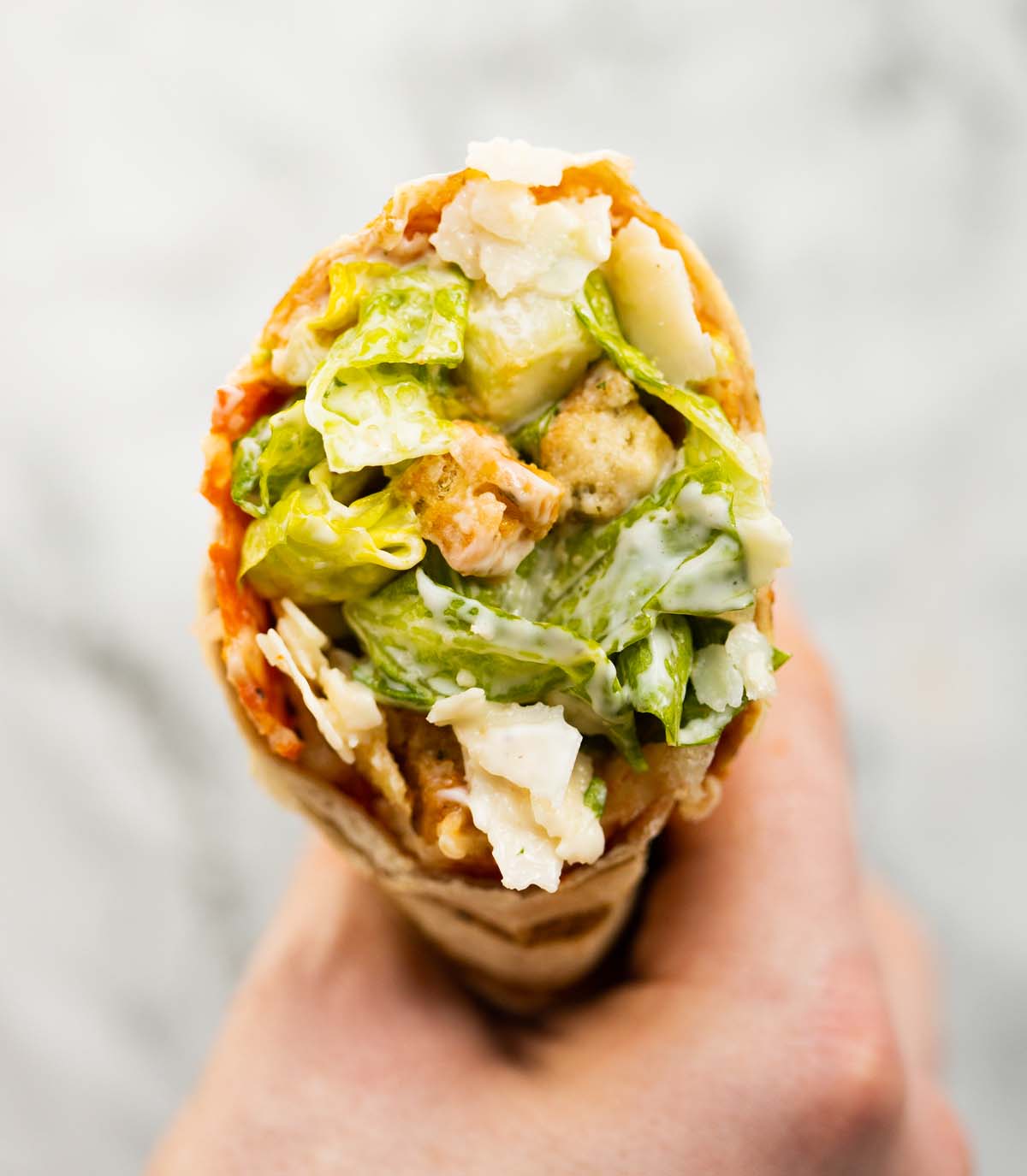 close up overhead shot of hand holding caesar salad pepperoni wrap