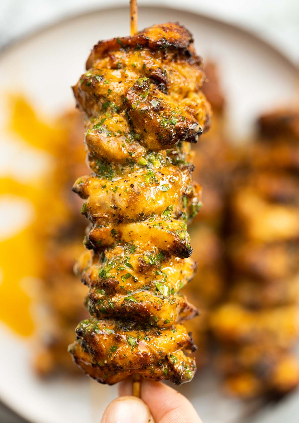 close up overhead shot of hand holding lemon butter chicken skewer